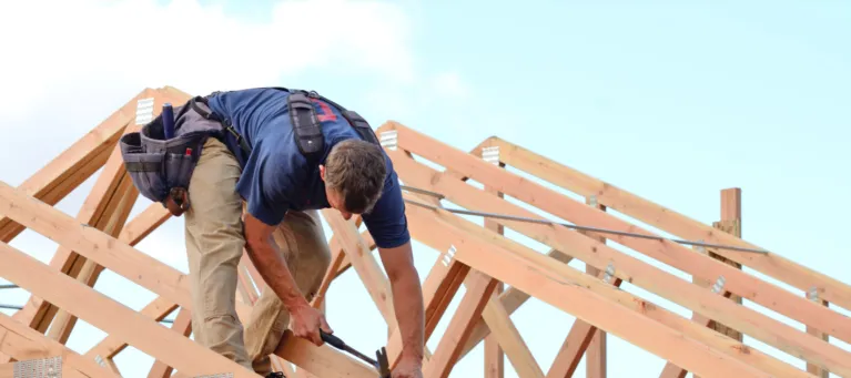 Worker on roof framework against a blue sky background.