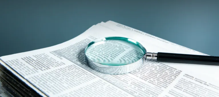 A magnifying glass rests on a stack of newspapers