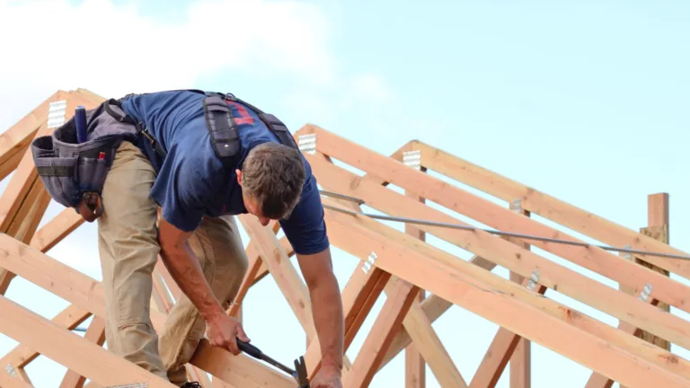 Worker on roof framework against a blue sky background.
