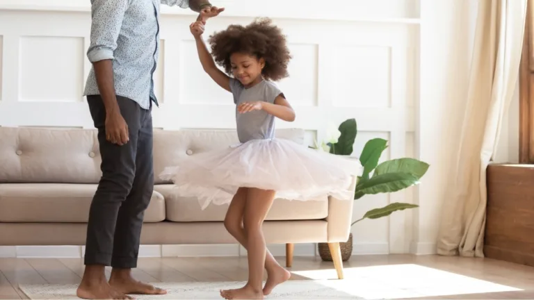 Man and young girl in tutu dancing in a living room, with an ad text for a philanthropic partner.