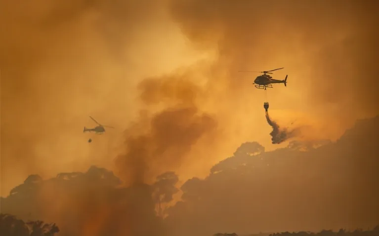 Image of two helicopters dropping water on fires in Los Angeles