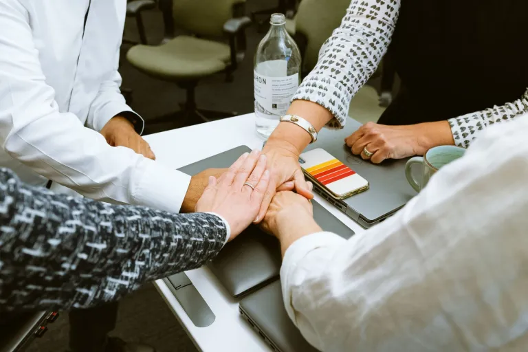 Image of 4 people placing their hands on top of each other, over computers