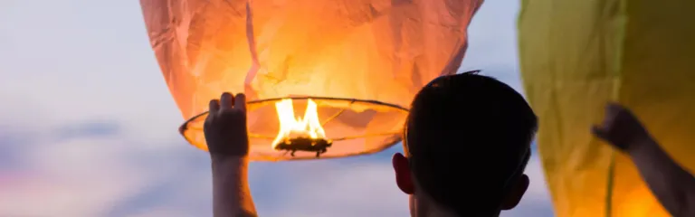 Man lifting orange lit lantern into the sky