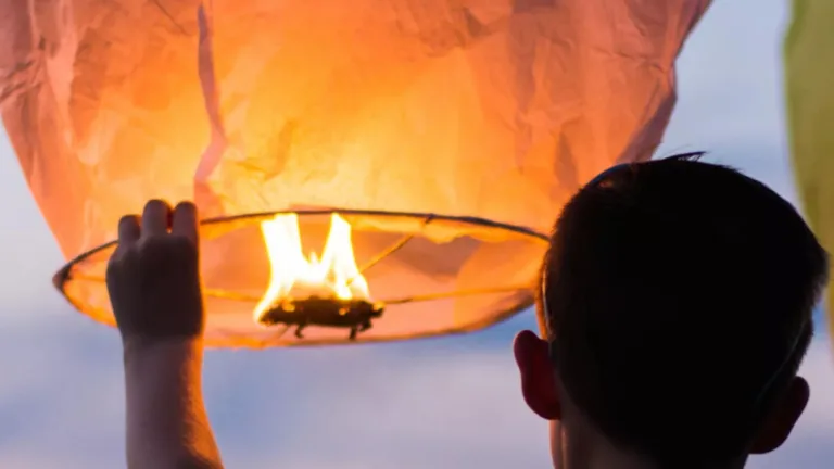 Man lifting orange lit lantern into the sky