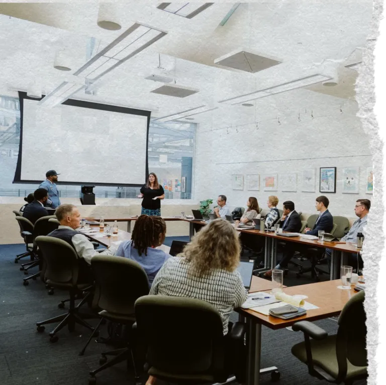 Torn paper image of people sitting in a conference room listening to a man and woman give a presentation