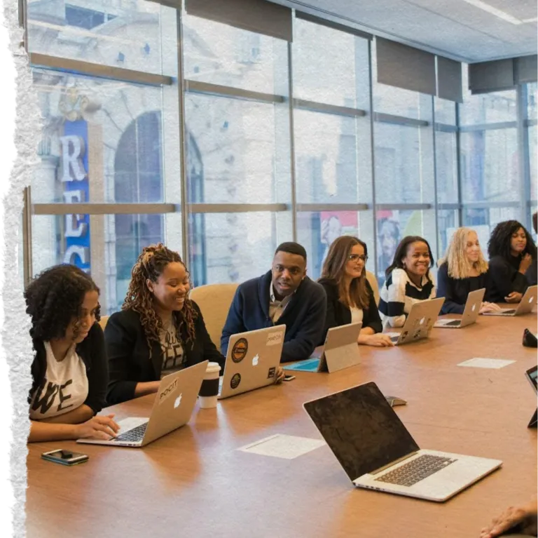 Torn paper image of workers at a conference table with laptops engaging in a meeting