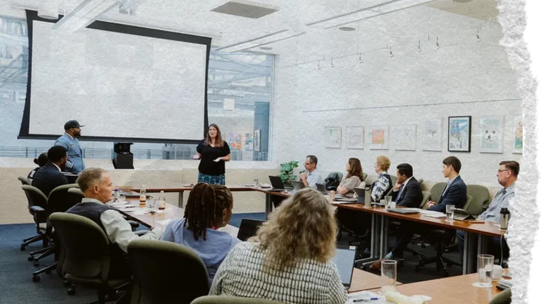 Torn paper image of people sitting in a conference room listening to a man and woman give a presentation