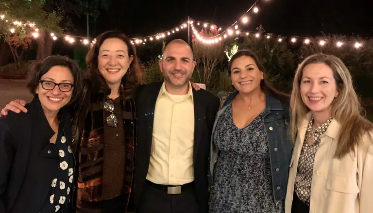 5 MCF team members smiling for group photo outdoors at night with string lights hanging in the background