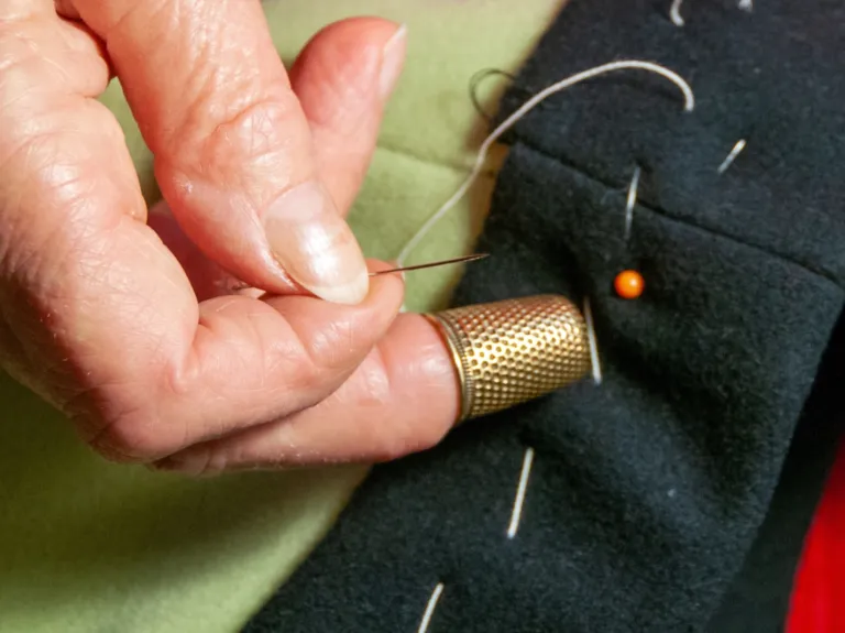 Close-up of a hand sewing fabric with a needle and thimble, pins in background