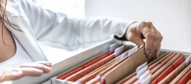 Person browsing through files in a filing cabinet drawer.