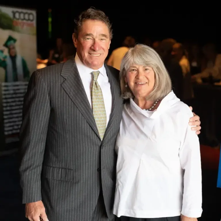 Two people embracing, one in a gray pinstripe suit and the other in a white blouse.