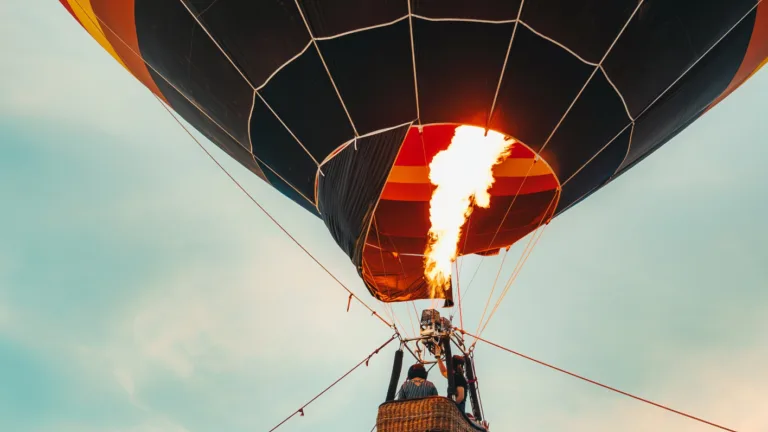 Hot air balloon with flame heating air against a blue sky.