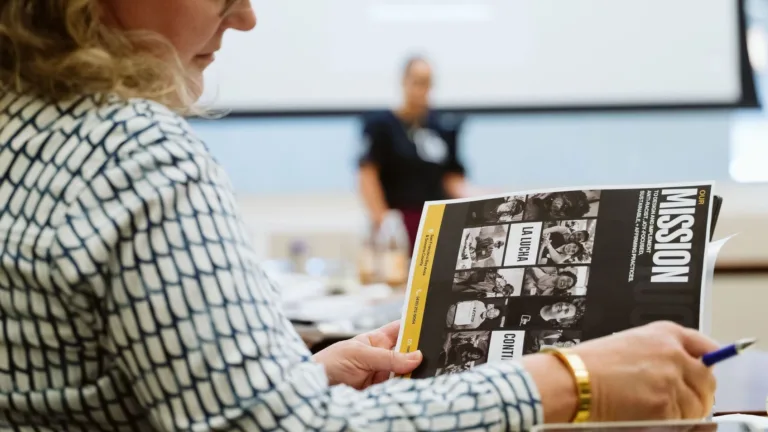 A woman with glasses and a white shirt flips through a magazine with a header that reads "Mission"