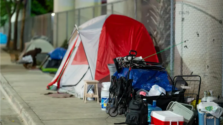 A sidewalk lined with tents and assorted belongings, indicating an urban homeless encampment.