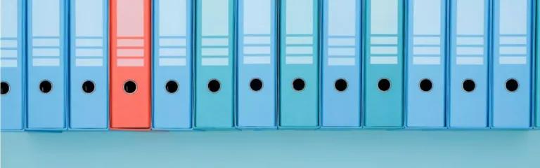 Row of blue binders with one red binder on a shelf.