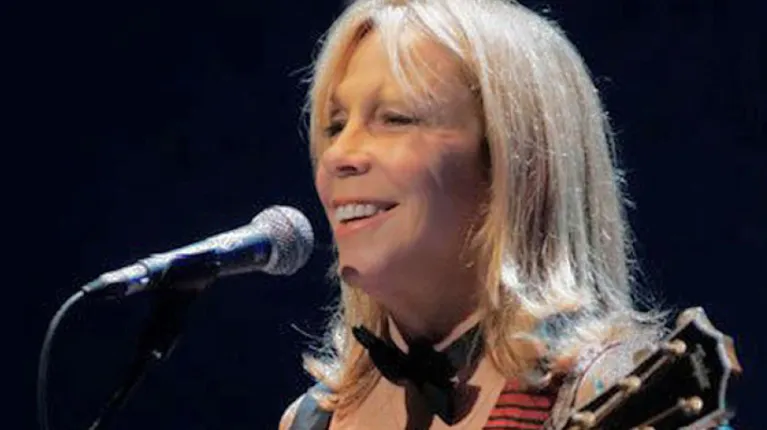 Woman with guitar in front of a microphone on a stage.