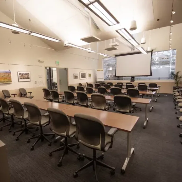 Empty room with chairs, tables, and a projection screen at the front.