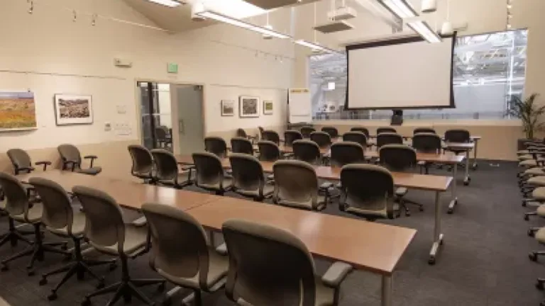 Empty room with chairs, tables, and a projection screen at the front.