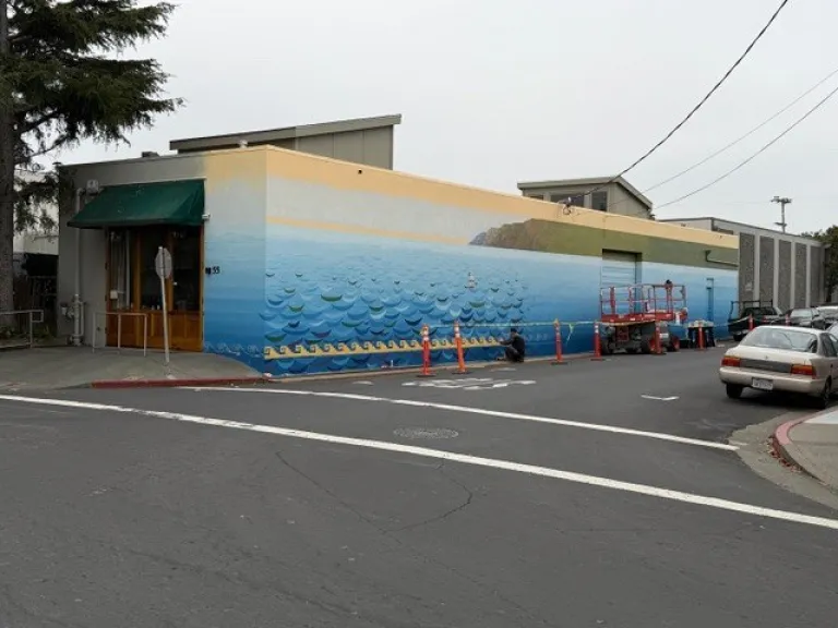 Image of a street in the Canal district of San Rafael with a building on the corner having a mural of the coastline painted on it