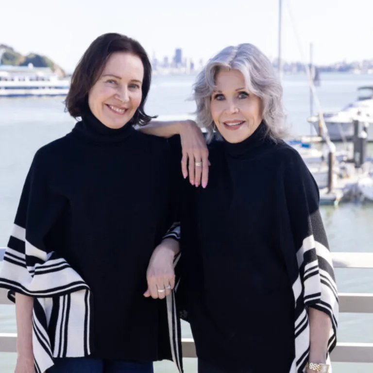 Jane Fonda and woman in black tops by the marina on a sunny day.