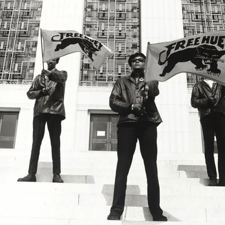 Image of three members of the Black Panthers, holding flags on the steps of a courthouse