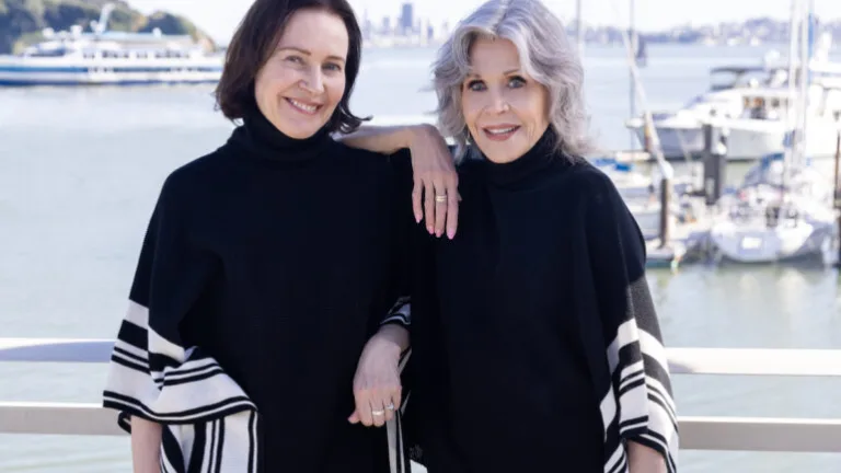 Jane Fonda and woman in black tops by the marina on a sunny day.