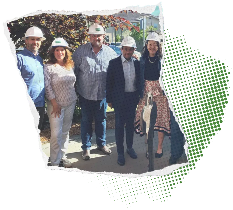 5 people in white hard hats, a mix of women and men, stand smiling and posed for the camera