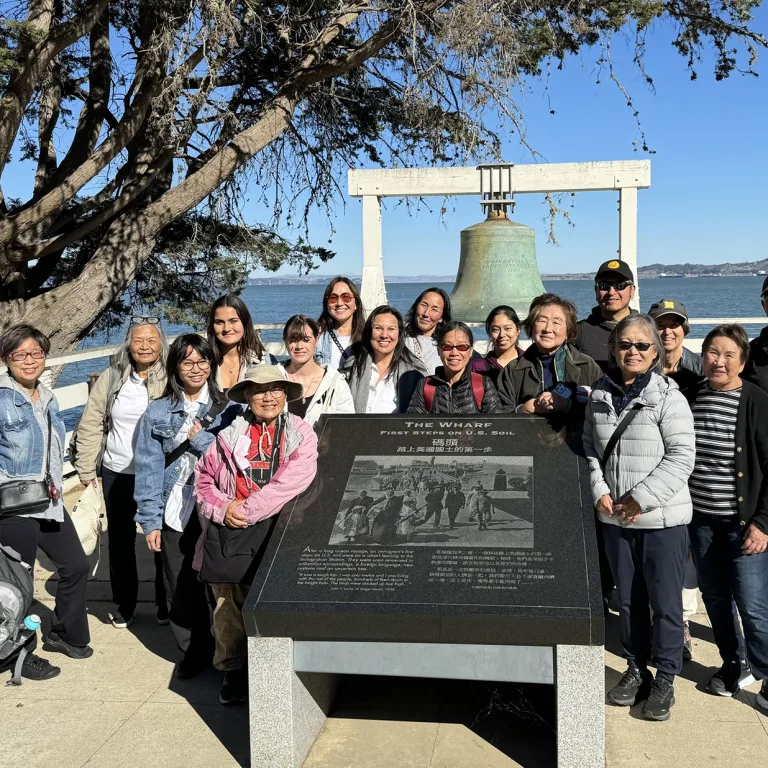 A group of Asian-Americans pose for a photo in front of a bell commemorating the immigration to Angel Island.