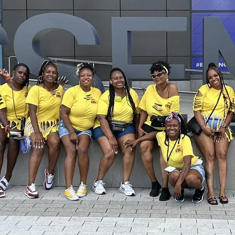 A group of black women stand together, posing for a photo in matching bright yellow t-shirts.