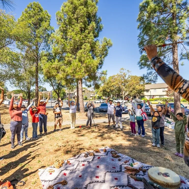 A diverse group of people stand together in a semi-circle with arms raised.