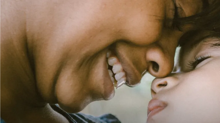 A close-up photo depicts the profile of a smiling mother, pressing the nose of her baby against her face