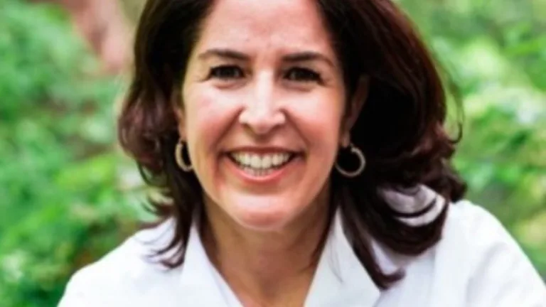 Head shot of Cavanagh smiling in a white blouse against green foliage