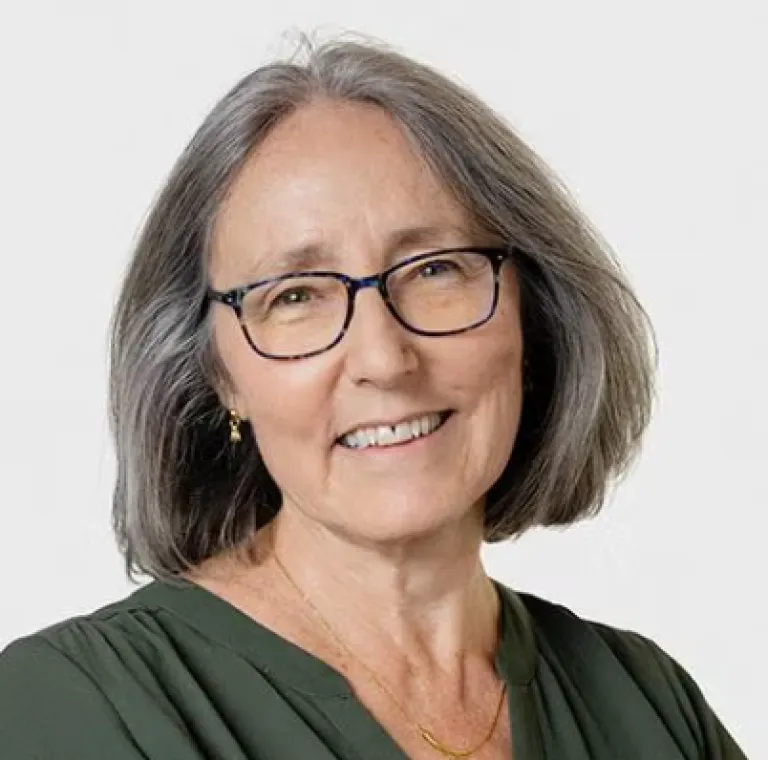 Image of Betsy Campbell, cropped head and shoulders, smiling at camera, wearing glasses and a green shirt
