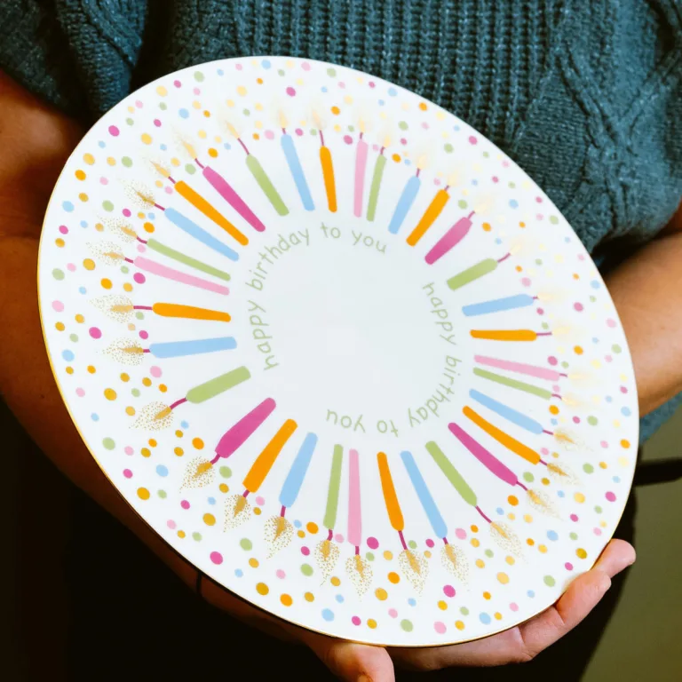 Person holding a colorful birthday plate with candles and "Happy Birthday to you" text design.