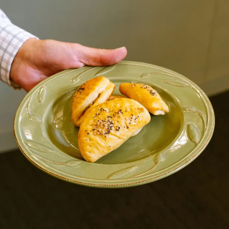 A person holding a green plate with three golden pastries topped with seeds.