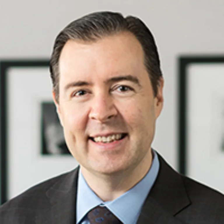 Headshot of Patrick McCabe wearing a light blue dress shirt, brown jacket, and brown tie