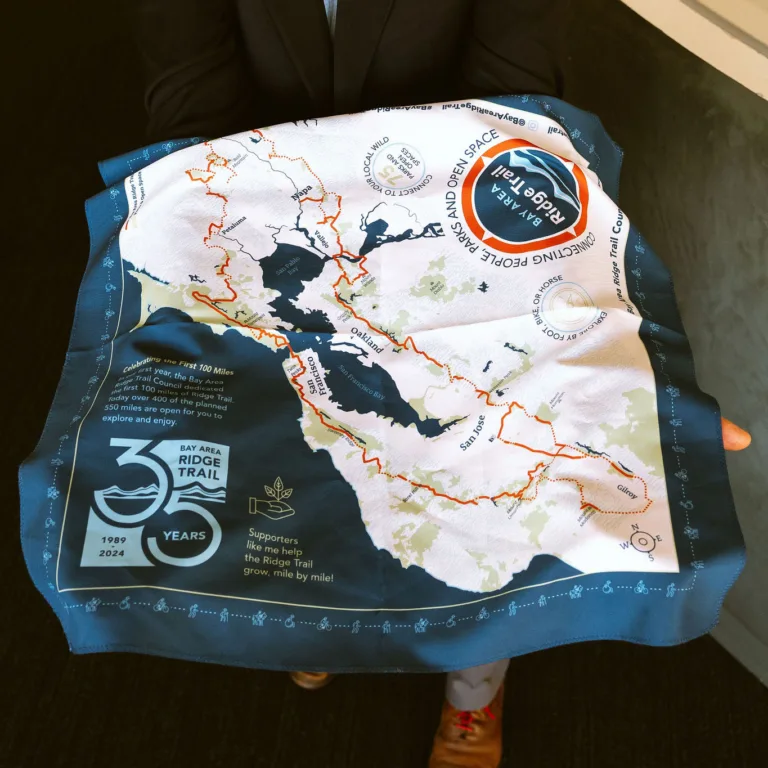 A person holds up a scarf with a map of the Bay Area Ridge Trail and event commemorative details.