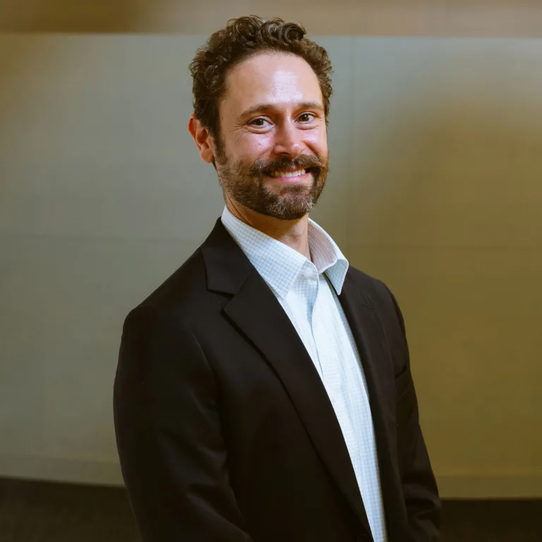 Headshot of Andy Kastner in a dark suit and light blue shirt standing against a neutral background.