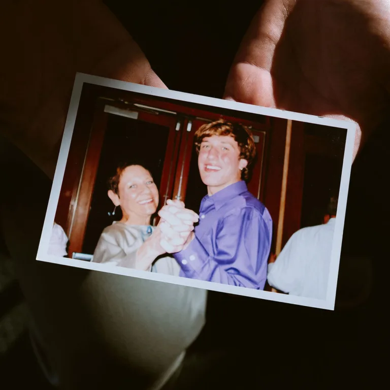 A person holding a Polaroid photo of two people against a dark background.