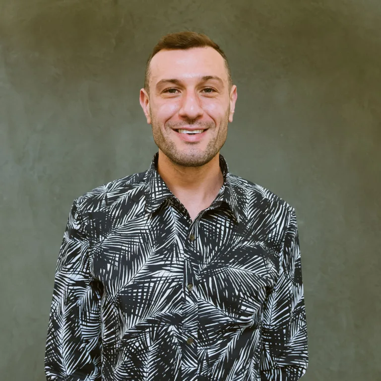 Headshot of Christian Moyer in a black and white patterned shirt standing against a green wall.