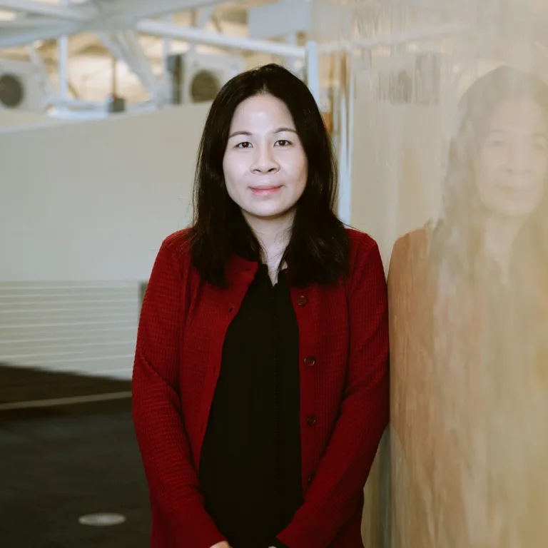 Headshot of Vickie Kuan in a red cardigan and black shirt standing indoors.