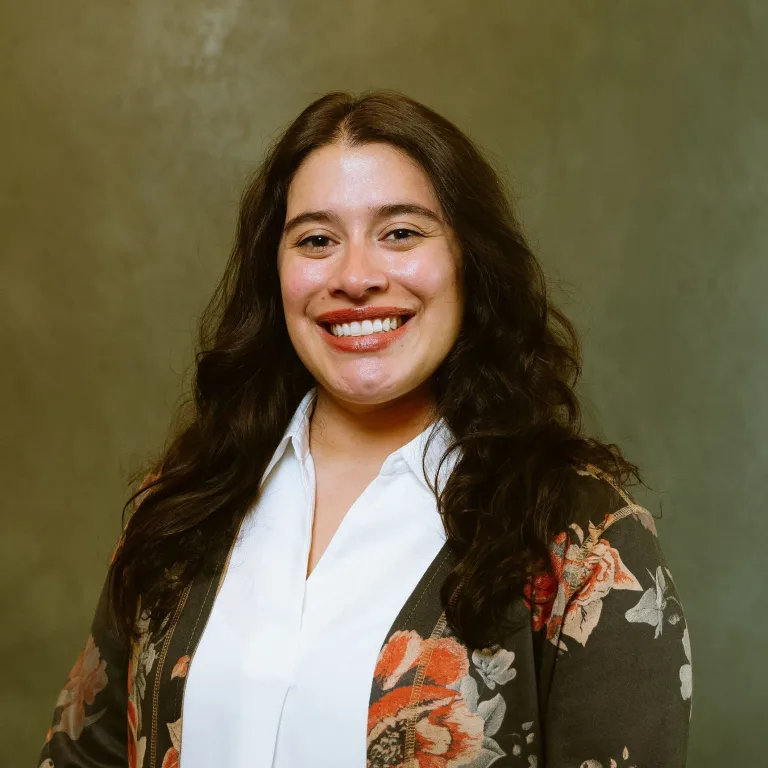 Image of Zayra Rivera, smiling at camera wearing a white shirt and floral jacket