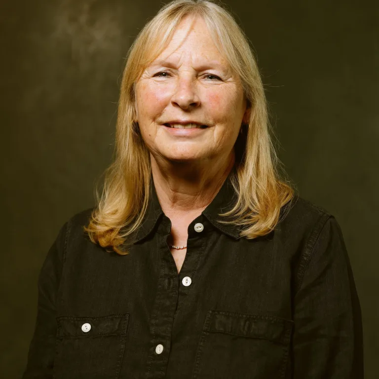 Image of Mary DiCarlo, smiling at camera, wearing a black shirt with white buttons