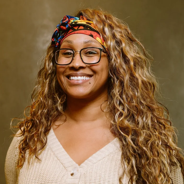 Image of Monique Bohman, smiling at camera, wearing glasses and a colored headscarf