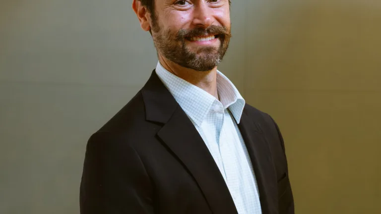 Headshot of Andy Kastner in a dark suit and light blue shirt standing against a neutral background.