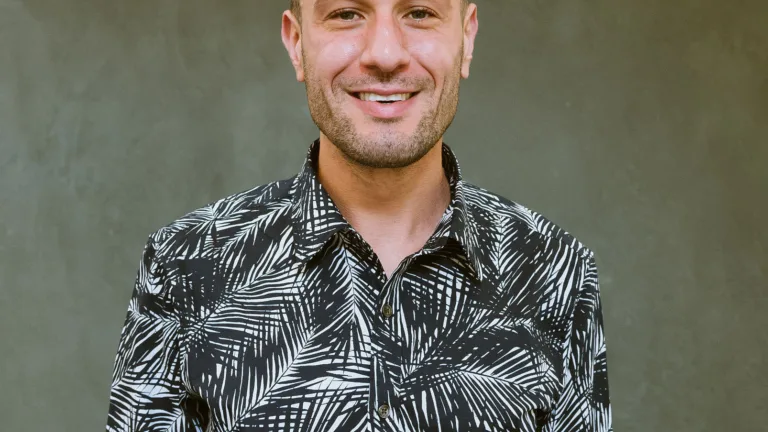 Headshot of Christian Moyer in a black and white patterned shirt standing against a green wall.