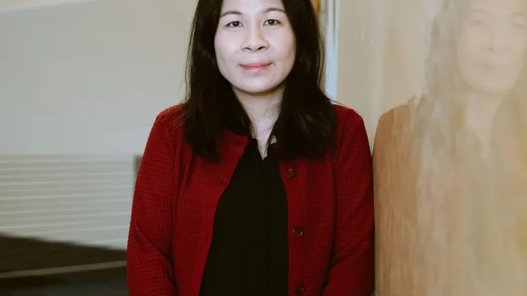 Headshot of Vickie Kuan in a red cardigan and black shirt standing indoors.