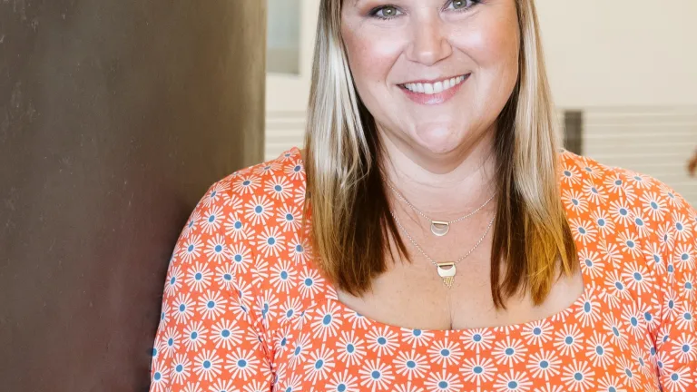 Image of Ashley Smith, leaning against a wall, smiling and wearing an orange and white top.